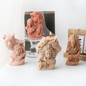May include: Three decorative candles with Native American themes. The candles are made of a beige wax and feature detailed carvings of a bear, a Native American warrior, and a Native American woman with a horse.
