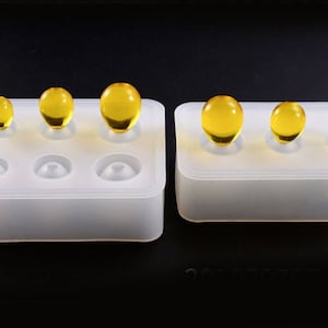 May include: Two white silicone moulds for making resin spheres. The moulds have three different sized cavities. The moulds are filled with yellow resin spheres.