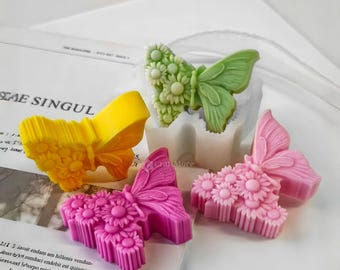 May include: Four silicone molds for making butterfly-shaped soaps or candles. The molds are in the shape of butterflies with daisy-like flowers on their wings. The butterflies are in pink, green, and yellow.