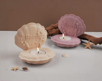 Op de afbeelding: Twee keramische schelpvormige kaarshouders met het woord "Beach" erop. De kaarshouders zijn roze en beige en hebben een klein theelichtje erin.