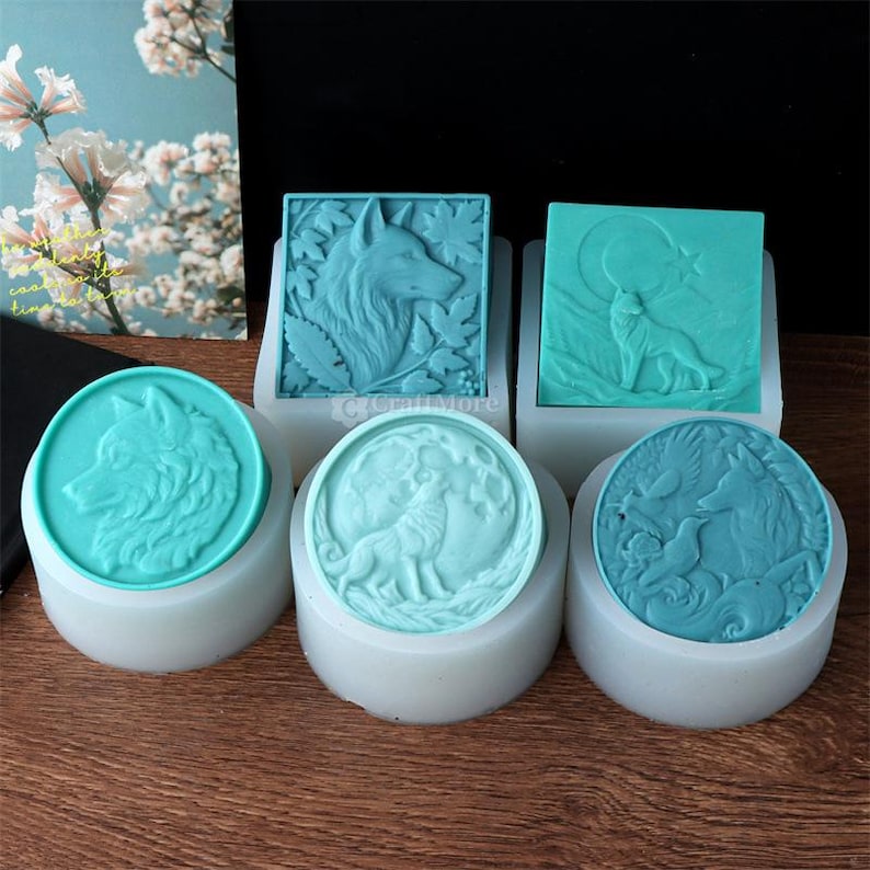 May include: A collection of turquoise silicone molds featuring wolf designs. The molds include square and circular shapes, with detailed wolf profiles, howling wolves, and nature-inspired elements. Ideal for soap making or crafting.