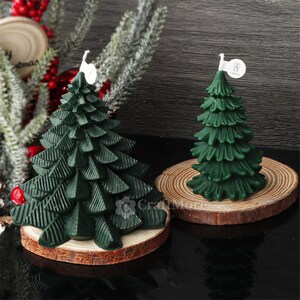May include: Two green pine tree shaped candles on wooden bases. The candles are decorated with a textured pine tree design.