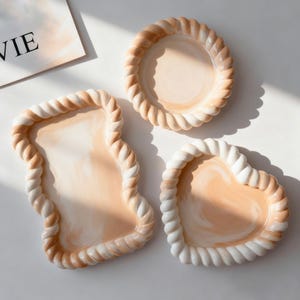 Può includere: Tre piatti da portata in ceramica in una palette di colori neutri. Il set comprende un piatto rotondo, un piatto a forma di cuore e un piatto rettangolare dalla forma unica. Ogni pezzo presenta un bordo a forma di corda nei toni crema e beige.