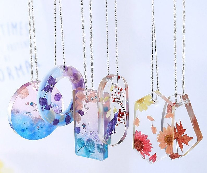 May include: Five silver chains with different pendants featuring pressed flowers and leaves encased in clear resin. The pendants are shaped like circles, rectangles, and ovals.