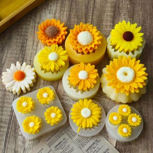 May include: A set of 10 silicone molds for baking sunflower-shaped cakes. The molds are arranged on a wooden surface with a few finished cakes in the molds. The cakes are yellow with a white center.