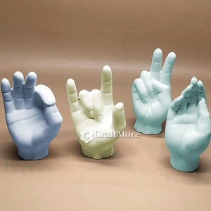 May include: Four ceramic hand sculptures in different hand gestures. The hands are in shades of light blue, light green, and cream.