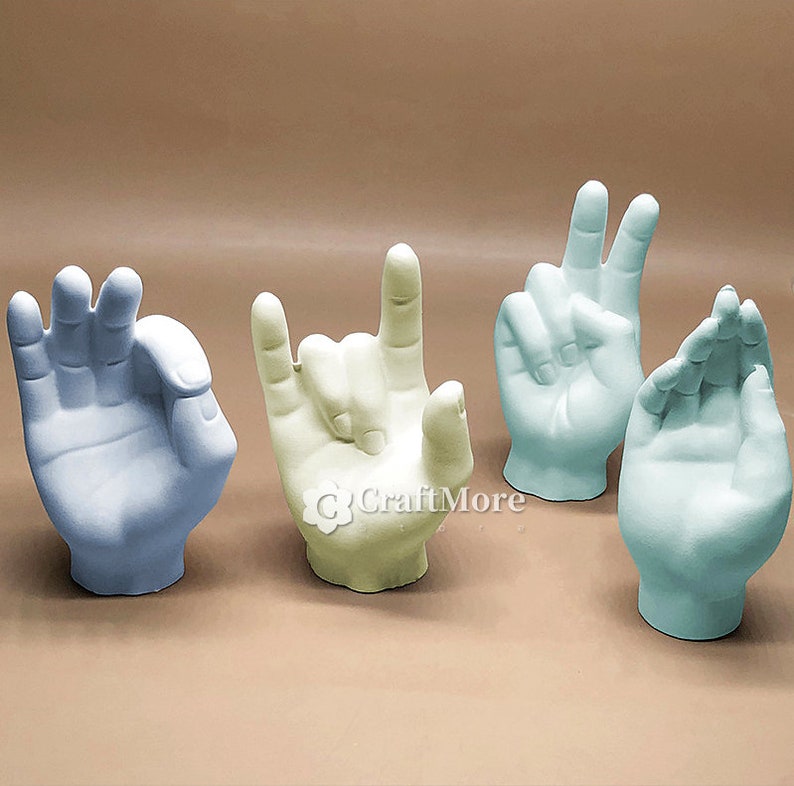 May include: Four ceramic hand sculptures in different hand gestures. The hands are in shades of light blue, light green, and cream.