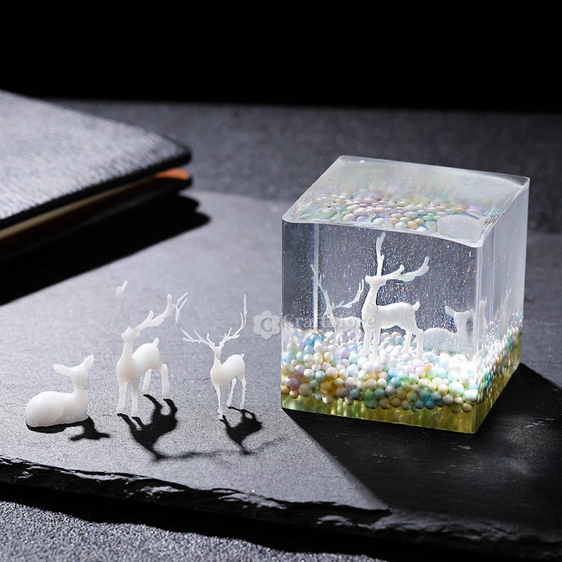 Pu&ograve; includere: Un cubo trasparente pieno di perline colorate e una statuetta di cervo bianca all'interno. Ci sono tre piccole statuette di cervo bianche all'esterno del cubo.