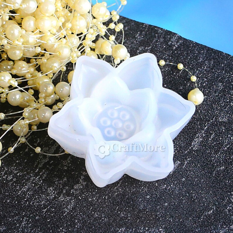 May include: White silicone mold shaped like a lotus flower with a circular center and six smaller circles inside. The mold is on a black surface.