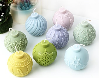May include: Eight decorative Christmas ornament candles in various colors and designs. The candles are shaped like ornaments and have different patterns, including snowflakes, trees, and swirls.