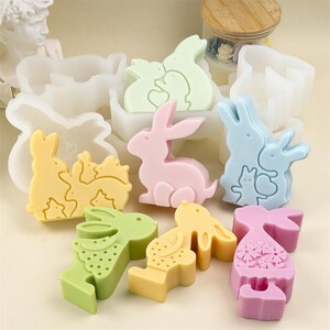 May include: A collection of colorful bunny-shaped soaps in various pastel shades, including pink, yellow, green, and blue. Some soaps feature multiple bunnies, while others have decorative patterns. The soaps are likely handmade and suitable for Easter.