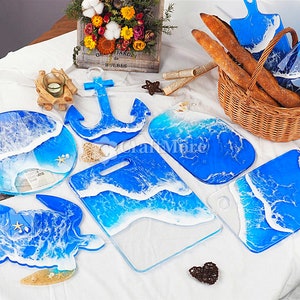Peut inclure: Un ensemble de neuf plateaux de service en résine avec des motifs d'ondes océaniques. Les plateaux sont de formes variées, notamment une tortue, une ancre et un rectangle. Tous les plateaux sont bleus et blancs avec des vagues blanches sur un fond bleu.