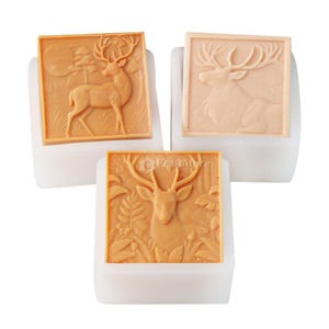 Pode incluir: Tr&ecirc;s moldes de sab&atilde;o quadrados, cor de bronzeado, com desenhos de veados. Um molde mostra um veado em p&eacute; numa cena de floresta, outro retrata um veado em repouso e o terceiro apresenta um veado com folhagem. Os moldes est&atilde;o em bases brancas.