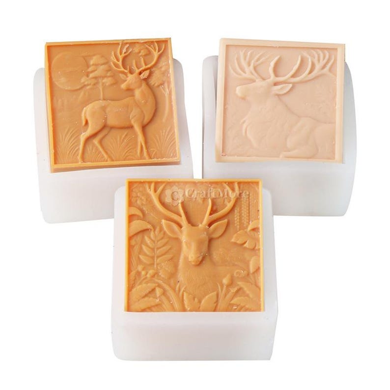 Pode incluir: Tr&ecirc;s moldes de sab&atilde;o quadrados, cor de bronzeado, com desenhos de veados. Um molde mostra um veado em p&eacute; numa cena de floresta, outro retrata um veado em repouso e o terceiro apresenta um veado com folhagem. Os moldes est&atilde;o em bases brancas.