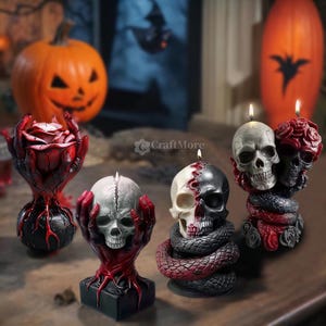 Op de afbeelding: Vier decoratieve schedelkaarsen met een Halloween-thema. De kaarsen zijn gemaakt van was en hebben een realistisch schedelontwerp. Twee van de kaarsen zijn omgeven door rode rozen en een zwarte slang. E&eacute;n kaars is omgeven door een rode roos en een zwarte slang. De vierde kaars is omgeven door een zwarte slang.