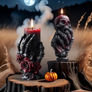 Może przedstawiać: Dwie świece o tematyce Halloween. Jedna to czarna świeca trzymana przez szkieletową dłoń z czerwonymi różami. Druga to świeca w kształcie czaszki trzymana przez szkieletową dłoń. Pomarańczowa dynia stoi na drewnianej powierzchni.