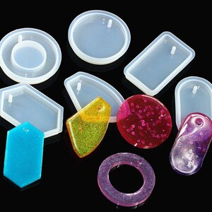 May include: A set of clear silicone molds for making jewelry. The molds are in various shapes, including circles, ovals, rectangles, and hexagons. Each mold has a small hole at the top for hanging the finished piece.