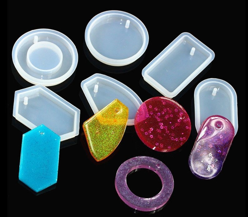May include: A set of clear silicone molds for making jewelry. The molds are in various shapes, including circles, ovals, rectangles, and hexagons. Each mold has a small hole at the top for hanging the finished piece.