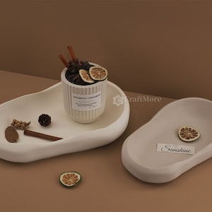 May include: Two white ceramic trays in an organic, asymmetrical shape. The larger tray has a small white ceramic jar with the text "Aromatic Cinnamon" on it. The smaller tray has a small piece of dried citrus fruit and a card with the text "Sunshine" on it.