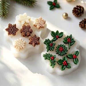 May include: Two white silicone molds for crafting. One mold contains six snowflake-shaped pieces in shades of cream and brown. The second mold features six holly leaf and berry clusters in green and red. The molds are flexible and translucent.