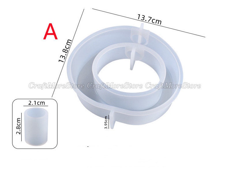 May include: A white silicone mold for making a two-tiered cake or dessert. The mold is 13.7 cm in diameter and 13.8 cm tall. It has a smaller inner ring that is 3.95 cm in diameter. The mold is shown next to a smaller silicone mold that is 2.1 cm in diameter and 2.8 cm tall.