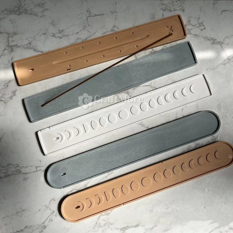 May include: Five incense stick holders in various colors, including beige, gray, and white. Each holder has a unique design with a series of circles and crescent moon shapes. The holders are made of a smooth, textured material.