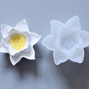 May include: A white silicone mold shaped like a lotus flower with a yellow center. The mold is used for making candles, soap, or resin crafts.