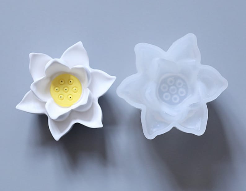 May include: A white silicone mold shaped like a lotus flower with a yellow center. The mold is used for making candles, soap, or resin crafts.