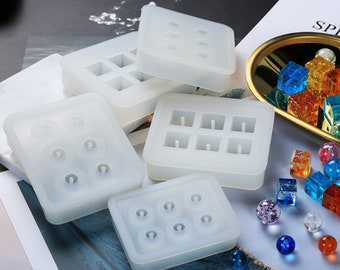 May include: Set of six white silicone molds for making resin jewelry. The molds are in various shapes, including squares, circles, and rectangles. Some molds have multiple cavities, while others have a single cavity.