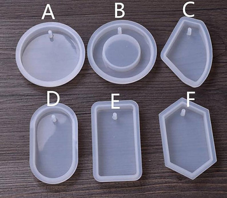 May include: Six clear silicone molds for making resin jewelry. The molds are shaped like a circle, oval, rectangle, hexagon, and two different teardrop shapes. Each mold has a small hole at the top for adding a bail or jump ring.