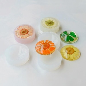 May include: Six round silicone moulds for resin crafts, with four filled with resin and pressed flowers. The moulds are clear and the resin is clear with a variety of pressed flowers, including a yellow daisy, an orange daisy, a white daisy, and a four-leaf clover.