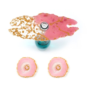 Könnte beinhalten: Ein Set aus drei Untersetzern aus rosa und goldenem Harz. Die Untersetzer sind in Form von Achat-Scheiben geformt und haben eine goldene Glitzer-Oberfläche. Das Set enthält einen Flaschenhalter mit zwei kleineren Untersetzern.