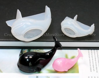 May include: Three silicone molds shaped like whales. The molds are white and are shown with black and pink whale figurines made with the molds.