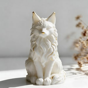 May include: A white fox figurine with gold accents. The fox is sitting upright with its paws together. The figurine has detailed fur and a gold nose and ear tips. The fox is a decorative item.