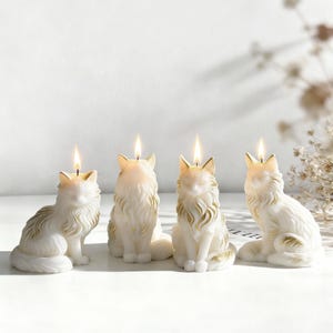 May include: Four white cat-shaped candles with gold accents and lit wicks. The candles are in various poses, with detailed fur and facial features. The candles are on a white surface, creating a soft, warm glow.