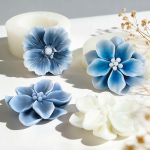 Könnte beinhalten: Vier blütenförmige Formen in verschiedenen Blau- und Weißtönen. Die Blumen haben detaillierte Blütenblattdesigns und einen zentralen Stempel. Eine Blume ist hellblau, eine andere dunkler blau und die letzte weiß.