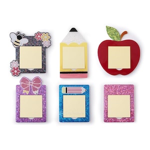 May include: Six decorative sticky note holders in various shapes. Designs include a bee with flowers, a pencil, a red apple, a bow, a pencil, and a pink glitter frame. Each holder has a square yellow sticky note.