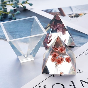 May include: Three clear resin molds for crafting. Two pyramid-shaped molds contain dried flowers. One square mold is a funnel shape.