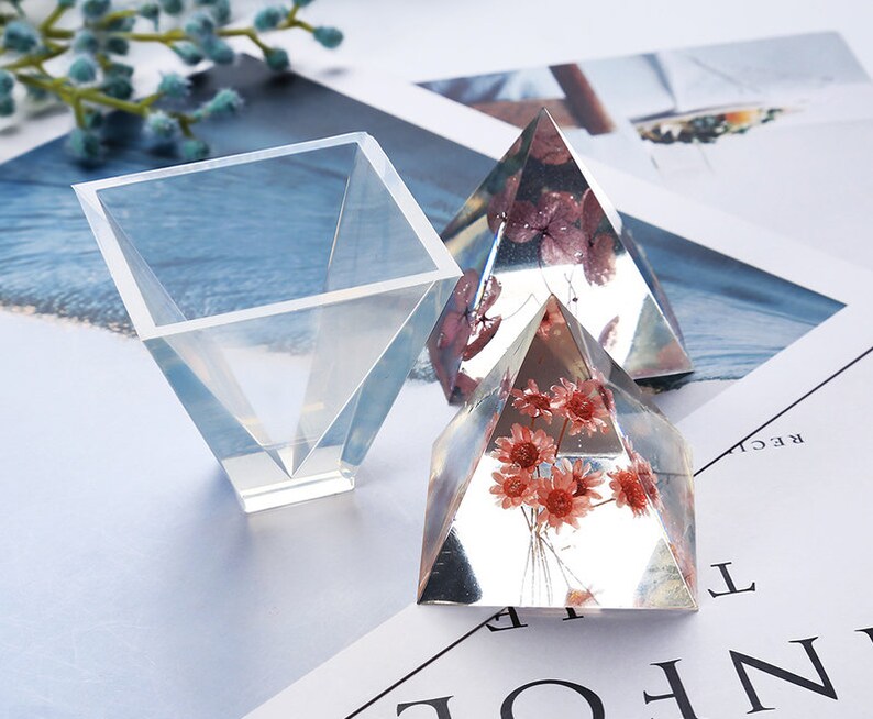 May include: Three clear resin molds for crafting. Two pyramid-shaped molds contain dried flowers. One square mold is a funnel shape.