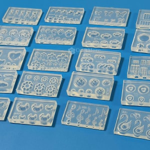 May include: A set of 16 clear silicone moulds for crafting. The moulds feature various designs, including flowers, hearts, musical notes, and geometric shapes.