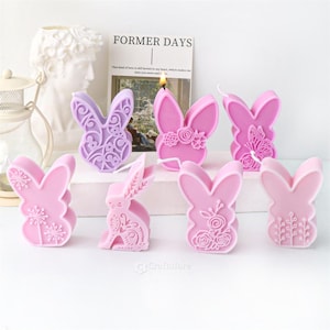 May include: Eight pink and purple bunny shaped candles with various floral and butterfly designs. The candles are arranged on a white surface. "Former Days" is written on a card in the background.