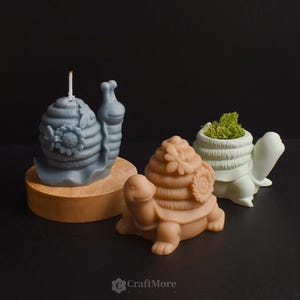 May include: Three decorative candles shaped like a snail, a turtle, and a turtle carrying a beehive. The snail candle is blue and has a flower design. The turtle candles are brown and green.