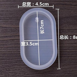 May include: A clear oval-shaped silicone mold with measurements in centimeters. The mold is 8 cm long, 7 cm tall, and 3.5 cm wide. The mold is on a wooden surface.