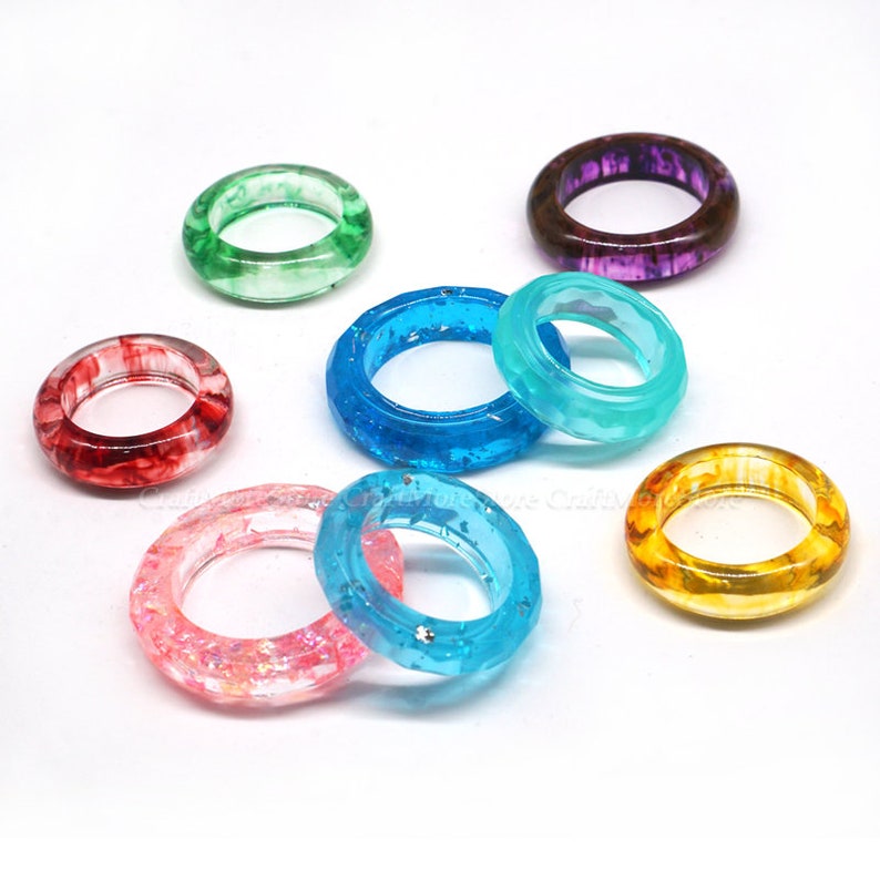 May include: Assortment of colorful resin rings with various patterns and textures. The rings are made of clear resin with embedded glitter, swirls, and marbling effects.