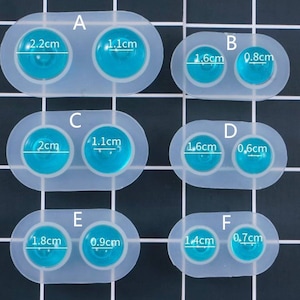 May include: A silicone mold with six pairs of round cavities for making resin jewelry. The cavities are labeled with letters A through F and measurements in centimeters. The mold is white and the cavities are filled with blue resin.