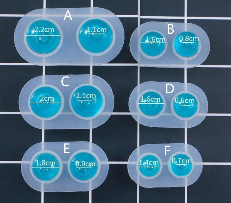May include: A silicone mold with six pairs of round cavities for making resin jewelry. The cavities are labeled with letters A through F and measurements in centimeters. The mold is white and the cavities are filled with blue resin.