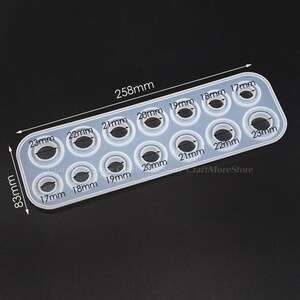 May include: A clear silicone mold with 10 round cavities of different sizes, ranging from 17mm to 23mm in diameter. The mold is 25.8 cm long and 8.3 cm wide. The mold is labeled with the size of each cavity in millimeters.