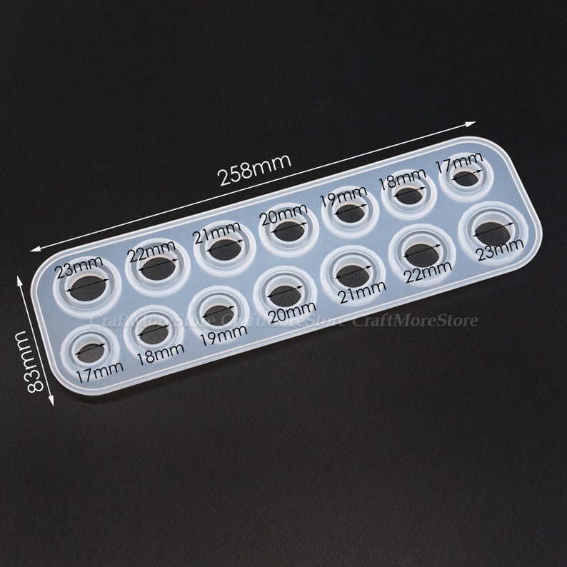 May include: A clear silicone mold with 10 round cavities of different sizes, ranging from 17mm to 23mm in diameter. The mold is 25.8 cm long and 8.3 cm wide. The mold is labeled with the size of each cavity in millimeters.