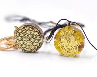 May include: Two gold-toned pendants on black cords. One pendant is round with a brown background and a gold geometric pattern. The other pendant is a yellow, faceted stone with a gold hamsa hand design.
