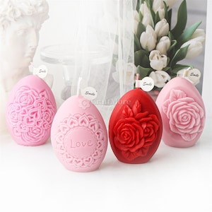 May include: Three pink and one red egg-shaped candles with floral designs. The pink candles have a rose and heart design, and the red candle has a rose design. The candles have the word "Smile" written on them.